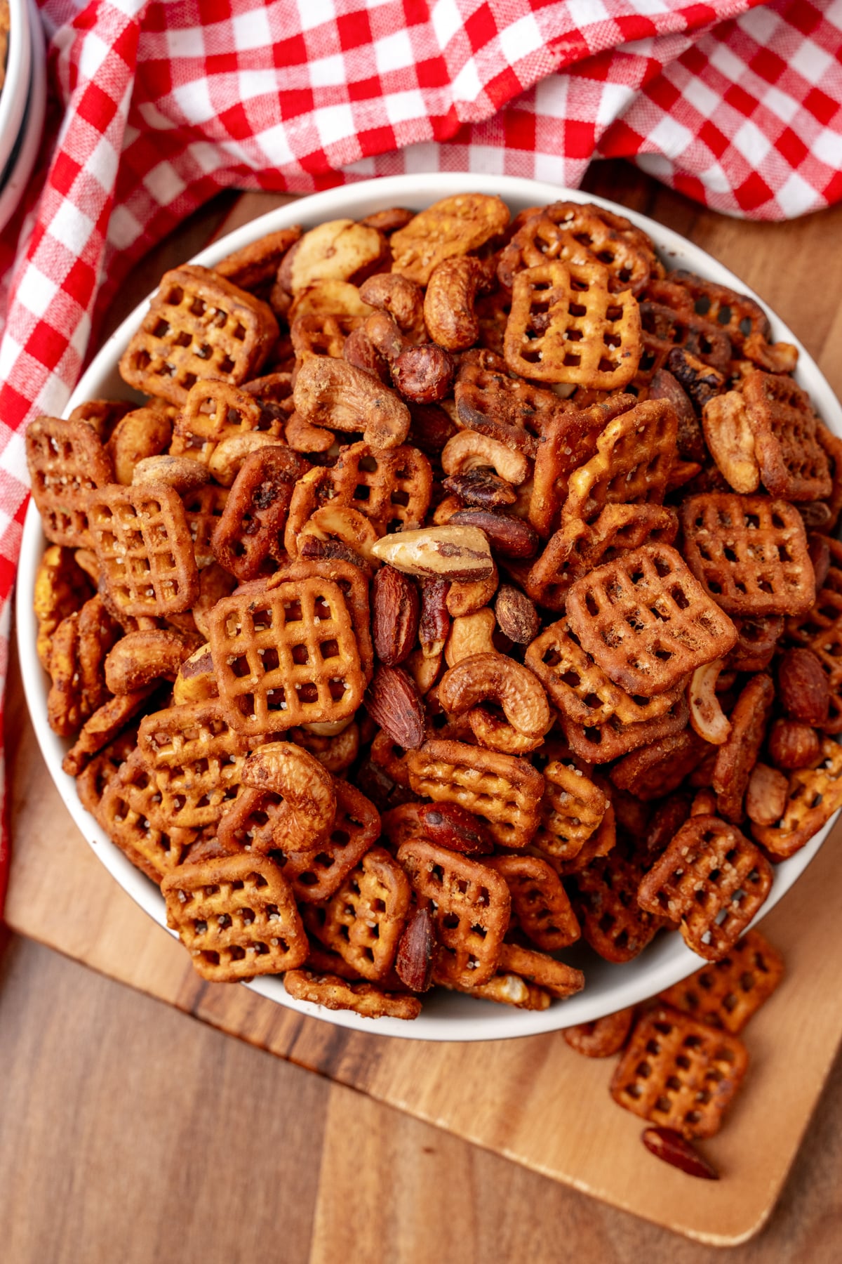 Buffalo snack mix 7 with waffle crackers and roasted nuts in white bowl on wooden board with red checkered cloth