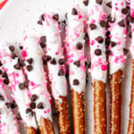 White chocolate-dipped valentines pretzels 4 topped with chocolate chips, pink sprinkles and pearl candies on white background