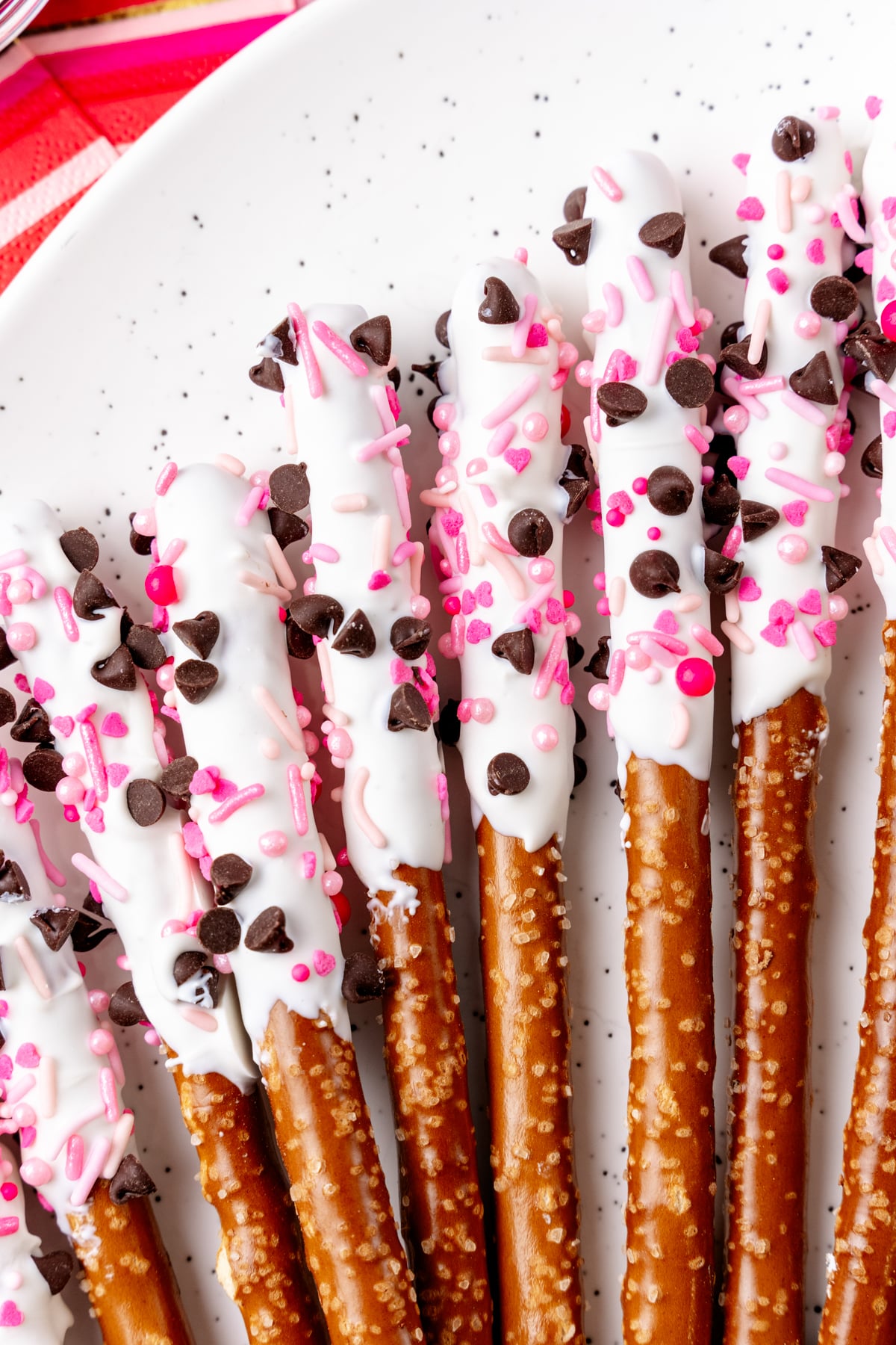 White chocolate-dipped valentines pretzels 4 topped with chocolate chips, pink sprinkles and pearl candies on white background