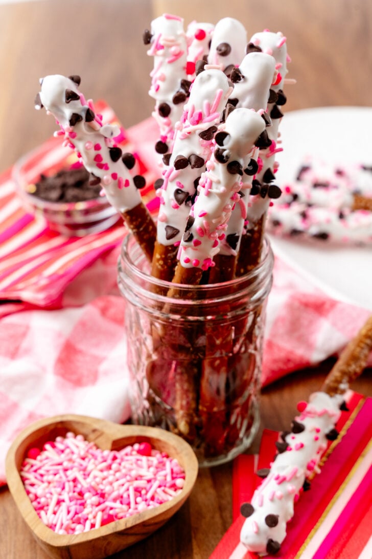 Jar filled with Valentines Pretzel Rods decorated with pink sprinkles and mini chocolate chips.