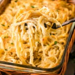 Fork lifting creamy baked fettuccini 8 from glass casserole dish in wicker basket with fresh parsley garnish