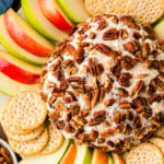 Party Cheese Ball with pecans on white plate surrounded by apple slices and crackers, overhead view