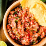 Fresh 5min salsa 7 in wooden bowl with tortilla chips, lime, cilantro and jalapeño on dark wood table