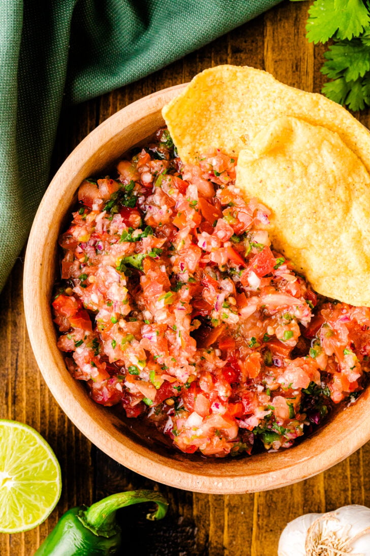 Fresh 5min salsa 7 in wooden bowl with tortilla chips, lime, cilantro and jalapeño on dark wood table