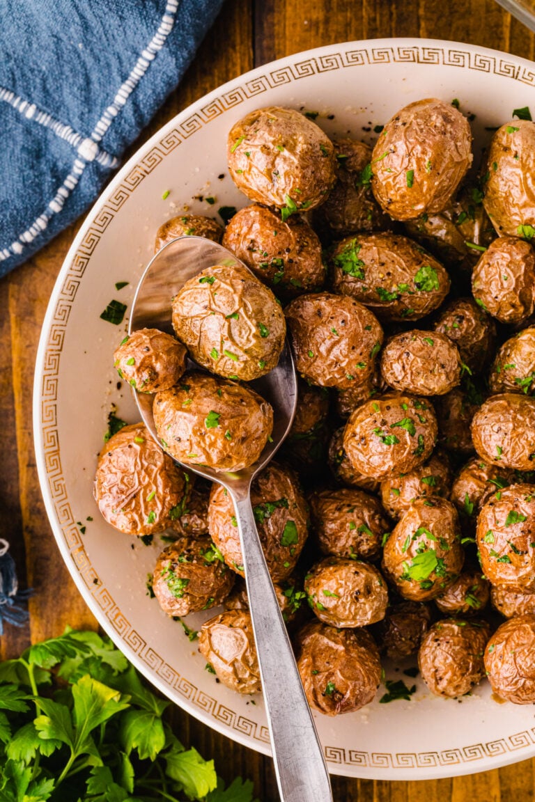 Roasted af baby potatoes 5 garnished with fresh parsley in cream bowl with gold Greek key pattern, served with spoon on dark wood table