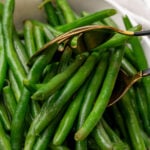 Golden fork lifting blanched green beans from white bowl with striped napkin, demonstrating How To Blanch Green Beans technique