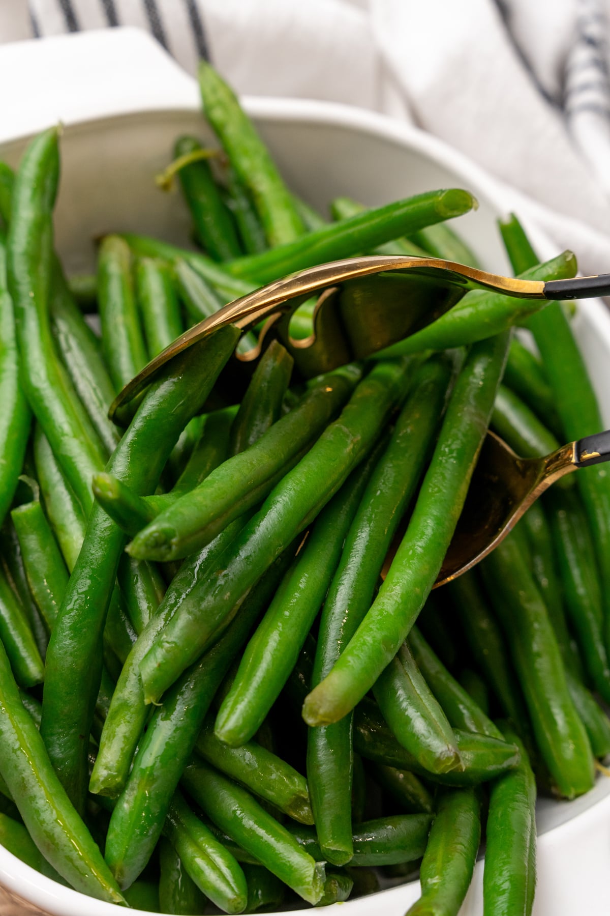 Golden fork lifting blanched green beans from white bowl with striped napkin, demonstrating How To Blanch Green Beans technique