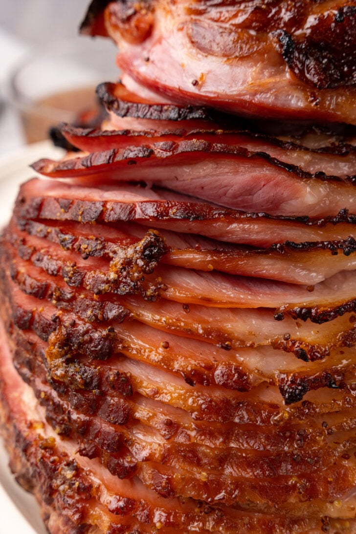 Close-up of a spiral-sliced, glazed ham with a golden-brown, crispy exterior. The layers reveal tender, juicy meat with caramelized edges, suggesting a savory and flavorful dish.
