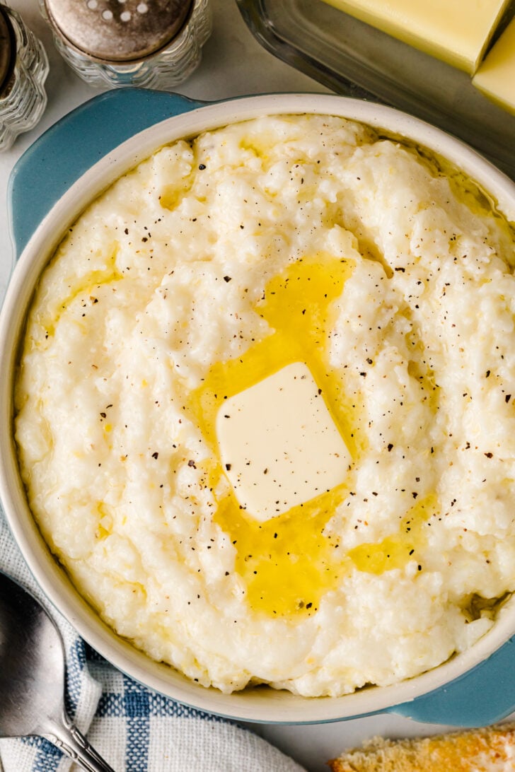 Crock Pot Southern Style Grits in white bowl with butter and black pepper garnish, overhead view
