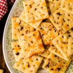 Homemade fire crackers 8 arranged on decorative plate with gold trim, topped with red pepper flakes and black seasoning, overhead view on wo