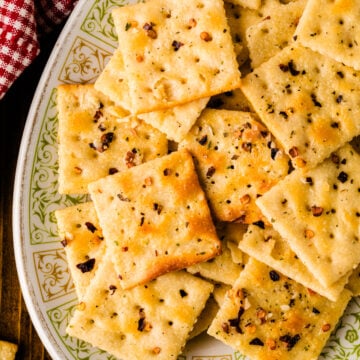 Homemade fire crackers 8 arranged on decorative plate with gold trim, topped with red pepper flakes and black seasoning, overhead view on wo