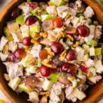 Waldorf Chicken Salad With Apples And Grapes served in wooden bowl with red grapes, walnuts, celery, and apples visible from above