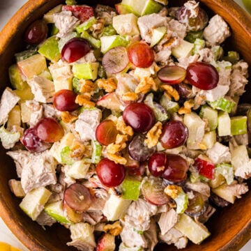 Waldorf Chicken Salad With Apples And Grapes served in wooden bowl with red grapes, walnuts, celery, and apples visible from above