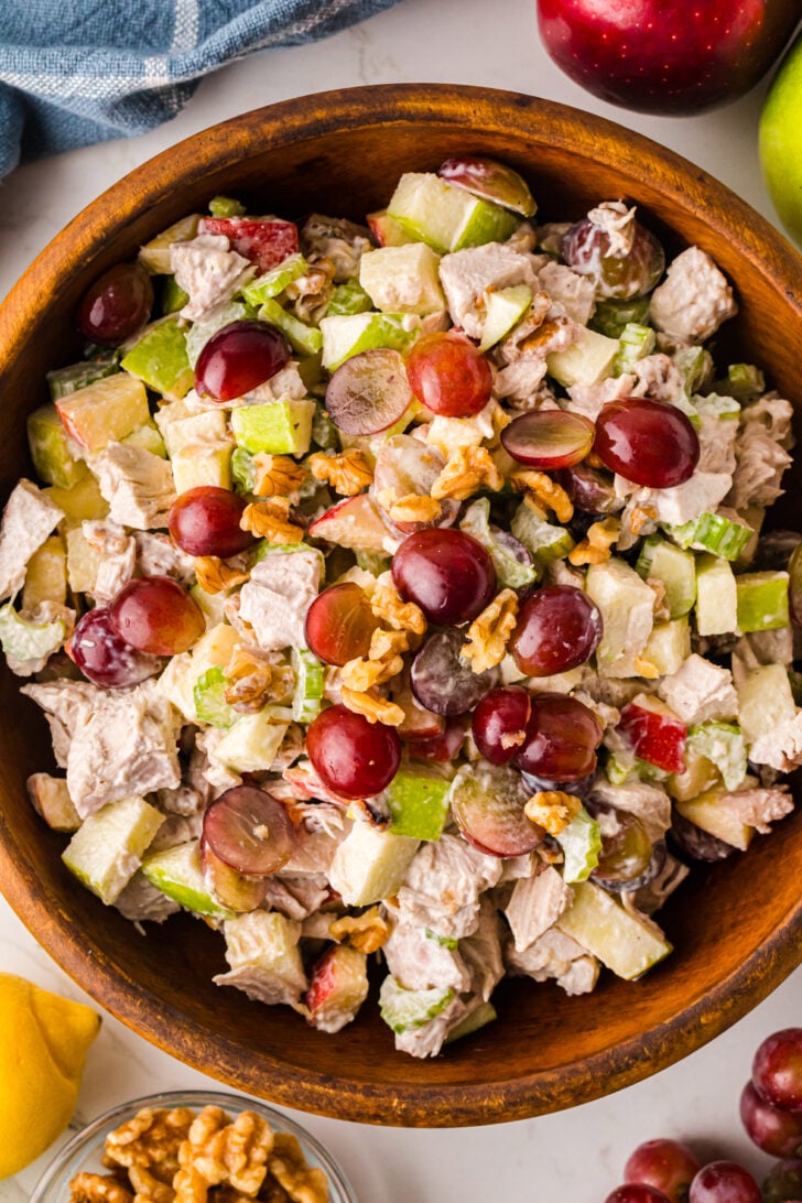 Waldorf Chicken Salad With Apples And Grapes served in wooden bowl with red grapes, walnuts, celery, and apples visible from above