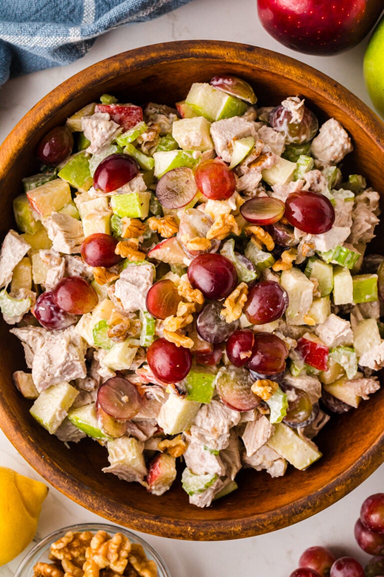 Waldorf Chicken Salad With Apples And Grapes served in wooden bowl with red grapes, walnuts, celery, and apples visible from above