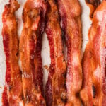 Crispy strips of bacon in oven 3 cooling on white paper towels, showing golden-brown and caramelized edges
