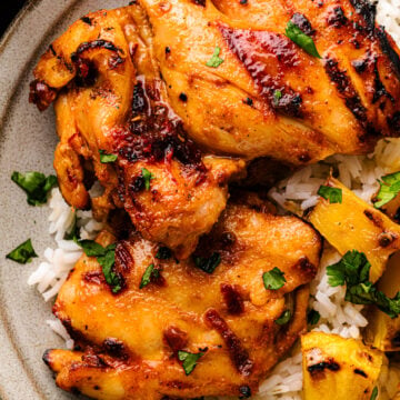 Honey Chipotle Grilled Chicken thighs with charred edges served on white rice with fresh cilantro garnish on a speckled ceramic plate