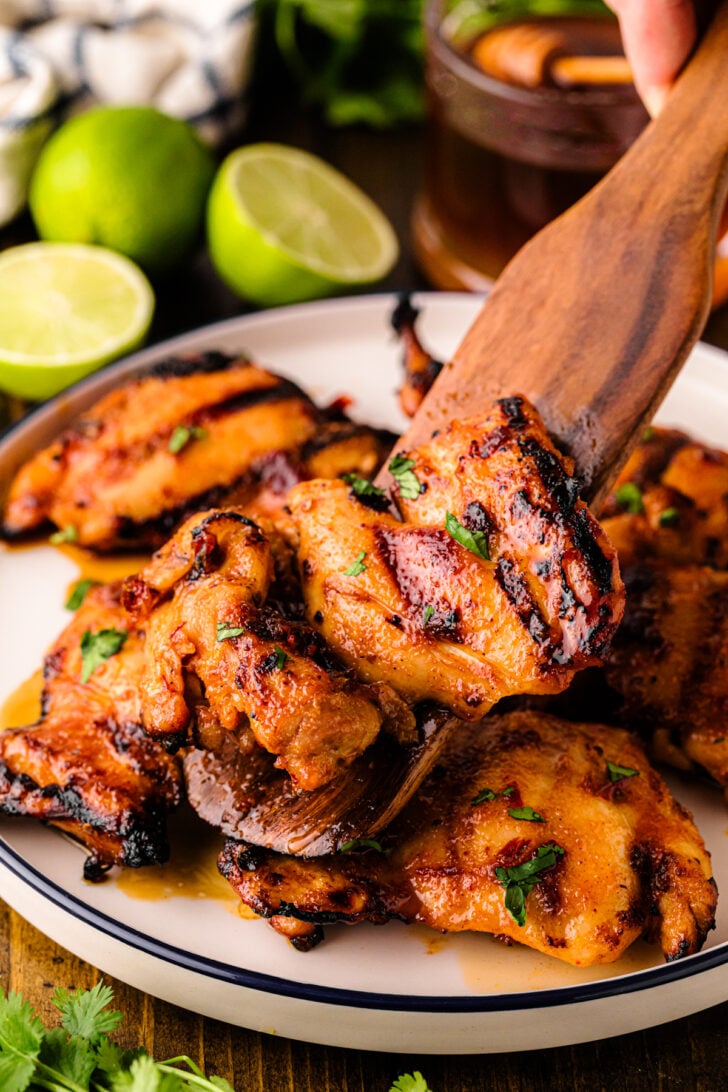 Honey Chipotle Grilled Chicken on white plate with lime wedges and cilantro garnish, wooden serving spoon lifting piece, charred edges visib