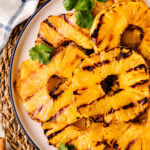 Grilled Pineapple with Brown Sugar Butter Glaze served on a white plate with navy rim, garnished with fresh cilantro
