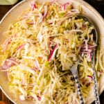 Southern Vinegar Slaw served on a decorative plate with pink radishes, cabbage, and serving utensils on a dark wood table