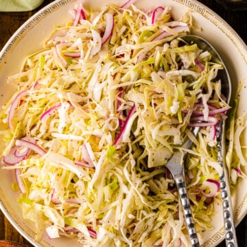 Southern Vinegar Slaw served on a decorative plate with pink radishes, cabbage, and serving utensils on a dark wood table