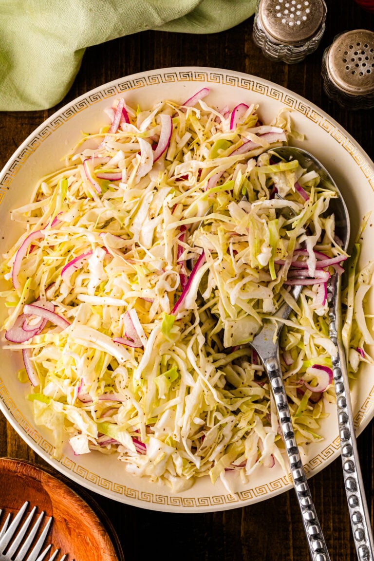 Southern Vinegar Slaw served on a decorative plate with pink radishes, cabbage, and serving utensils on a dark wood table