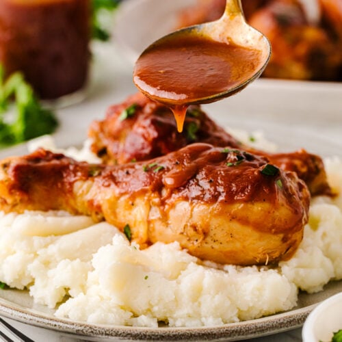 Crock Pot Chicken Legs with glossy brown sauce drizzled over mashed potatoes on a plate, garnished with fresh herbs