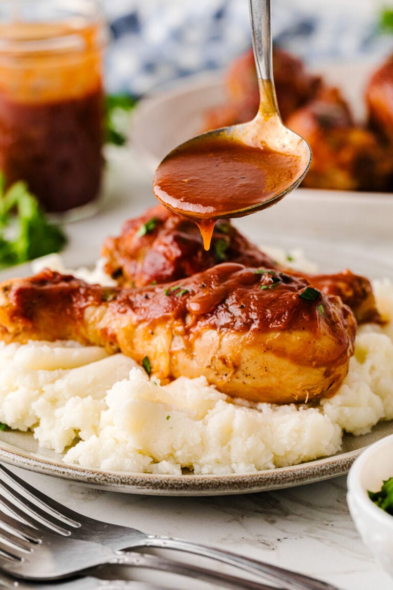 Crock Pot Chicken Legs with glossy brown sauce drizzled over mashed potatoes on a plate, garnished with fresh herbs
