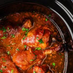 Crock Pot Chicken Legs in a slow cooker with glossy brown sauce and green onion garnish, overhead view