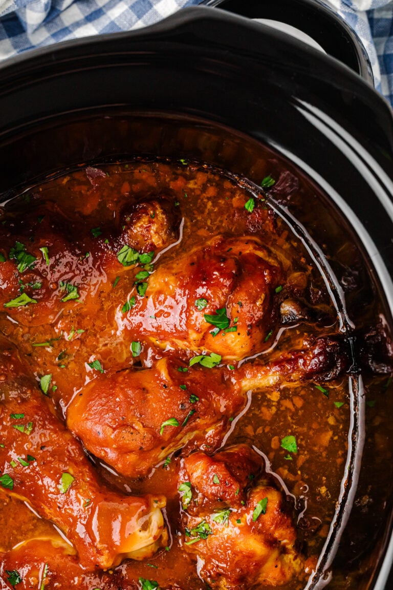 Crock Pot Chicken Legs in a slow cooker with glossy brown sauce and green onion garnish, overhead view