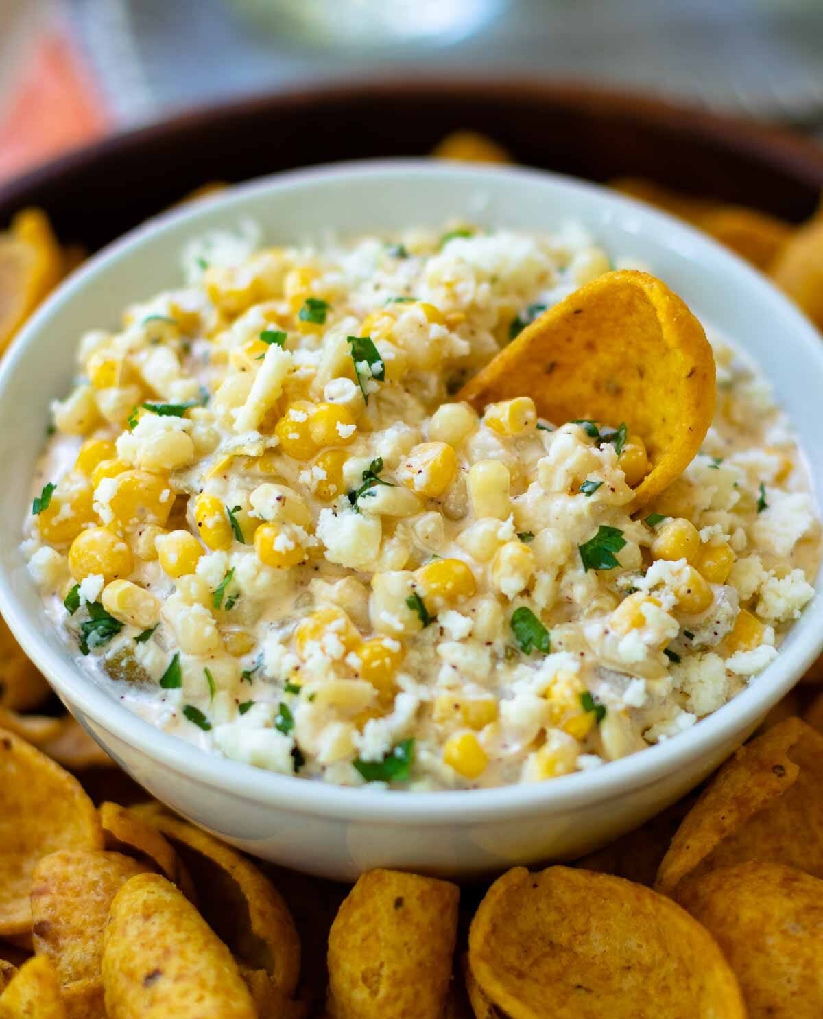Creamy corn dip with fresh herbs in white bowl surrounded by tortilla chips for party-perfect dips to share all summer long
