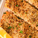 Oven Baked Pecan Crusted Salmon fillets in white baking dish with lemon wedges, garnished with fresh parsley