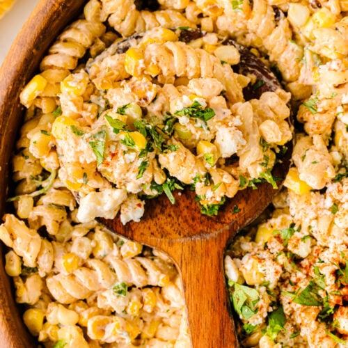 Mexican Street Corn Pasta Salad in wooden bowl with spoon, topped with fresh cilantro and seasoning, overhead view