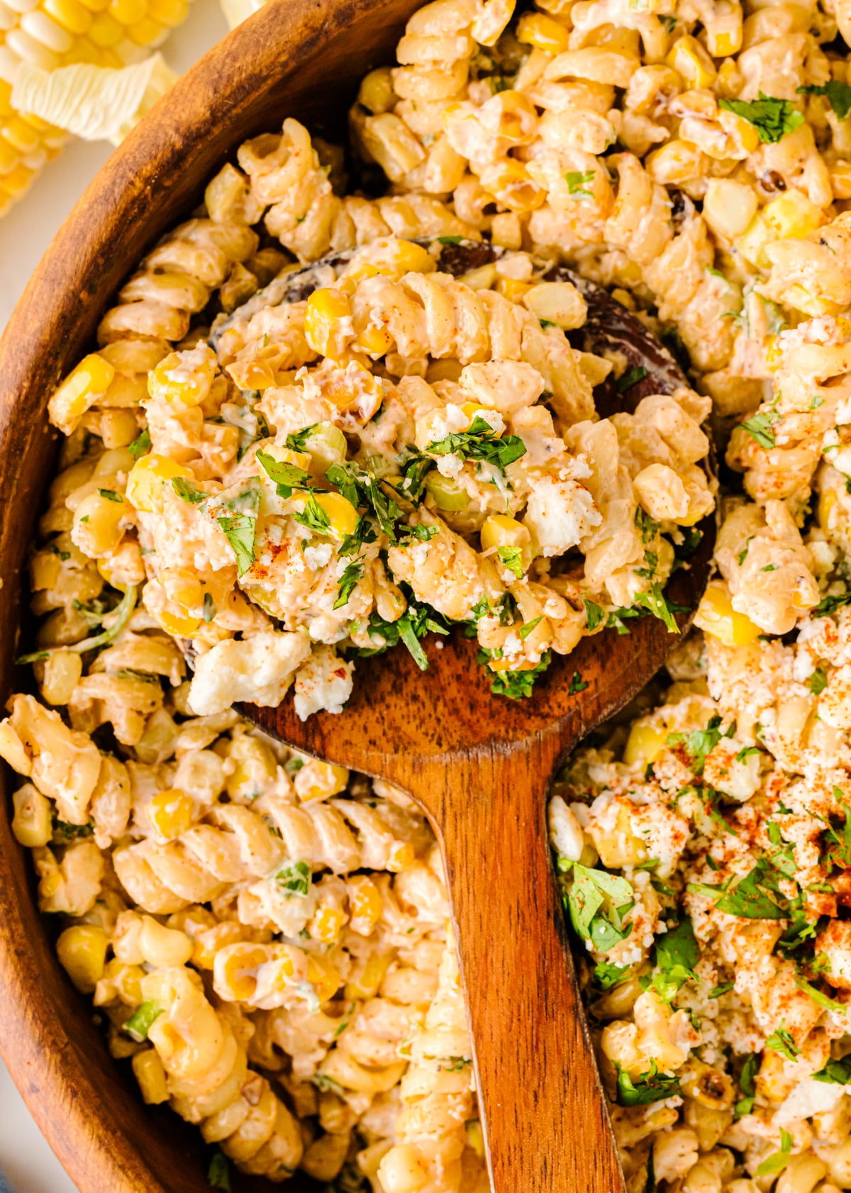 Mexican Street Corn Pasta Salad in wooden bowl with spoon, topped with fresh cilantro and seasoning, overhead view