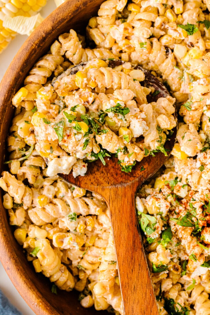 Mexican Street Corn Pasta Salad in wooden bowl with wooden spoon, topped with fresh cilantro and corn kernels
