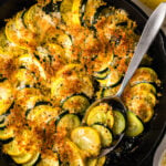 Golden-brown zucch squash casserole 8 in cast iron skillet with crispy breadcrumb topping and fresh yellow squash beside it