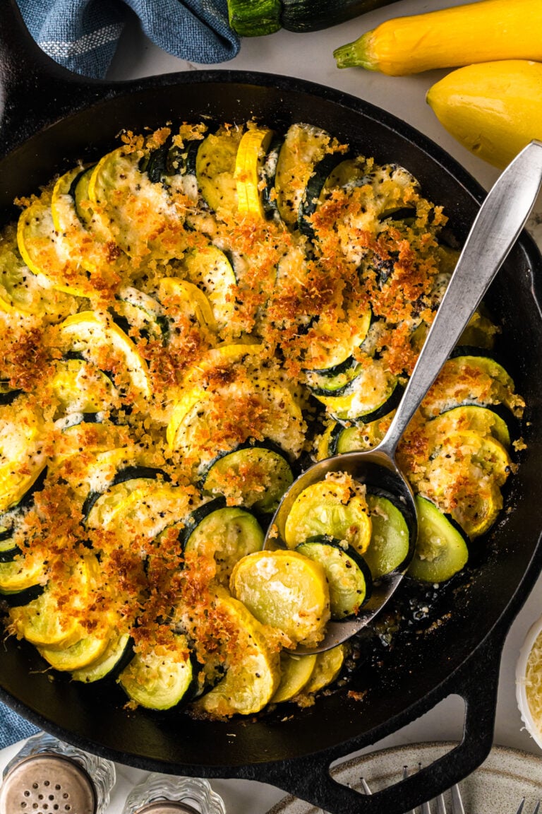 Golden-brown zucch squash casserole 8 in cast iron skillet with crispy breadcrumb topping and fresh yellow squash beside it