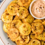 Crispy fried squash slices on white plate with creamy dipping sauce and red pepper flakes garnish
