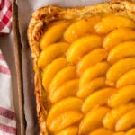 Golden baked peach tart 5 with caramelized fruit slices arranged in rows on parchment paper in wooden tart pan