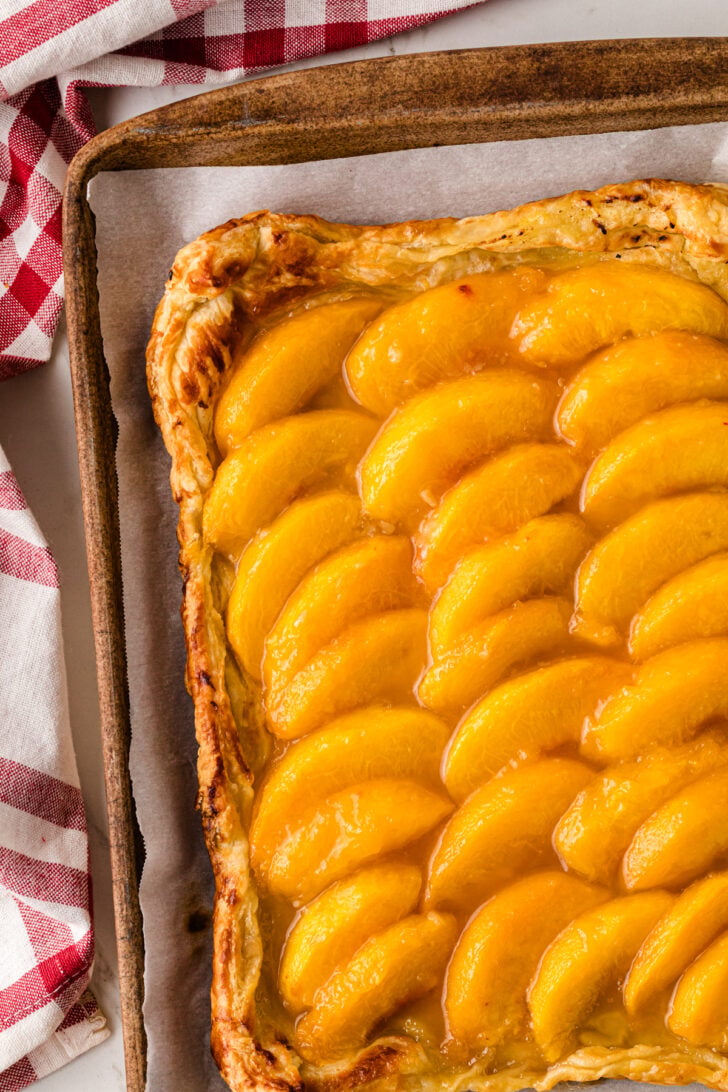 Golden baked peach tart 5 with caramelized fruit slices arranged in rows on parchment paper in wooden tart pan