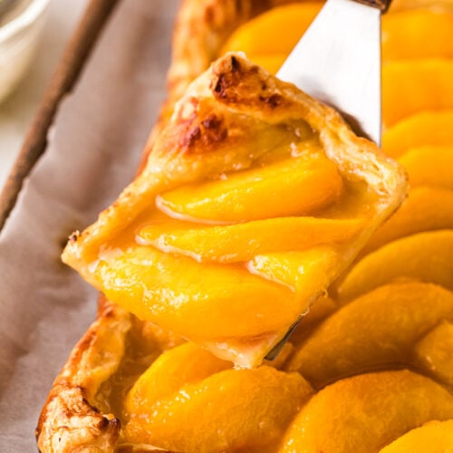 Close-up of a golden peach tart 7 with caramelized pastry crust, topped with glossy peach slices and a knife with wooden handle