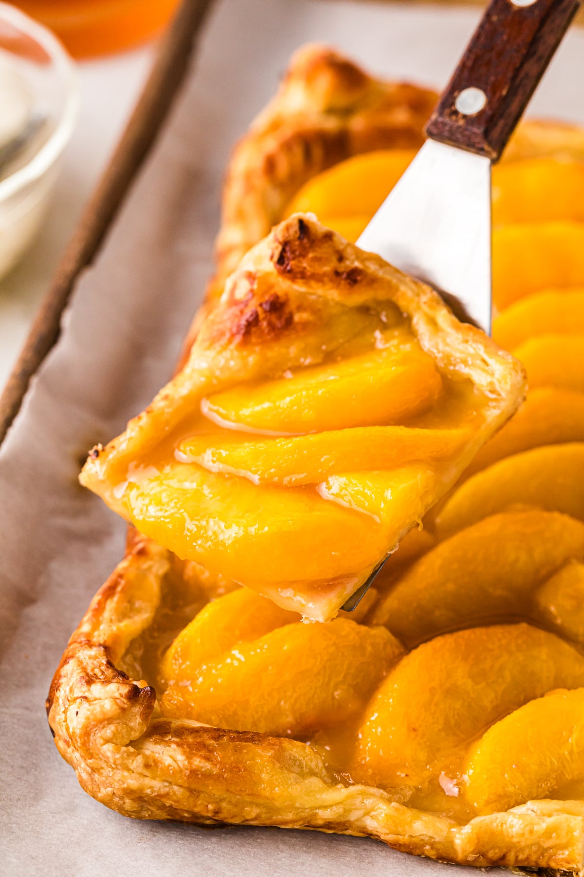 Close-up of a golden peach tart 7 with caramelized pastry crust, topped with glossy peach slices and a knife with wooden handle