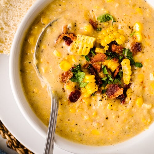 Creamy Corn Chowder in white bowl topped with bacon, corn, cilantro, and black pepper, served with bread slices