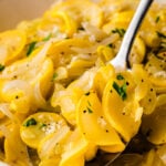Creamed squash and onions 10 in a white bowl with fresh parsley and black pepper garnish, served with a silver spoon