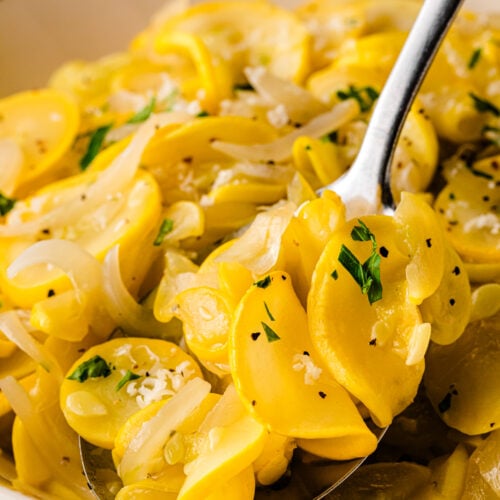 Creamed squash and onions 10 in a white bowl with fresh parsley and black pepper garnish, served with a silver spoon