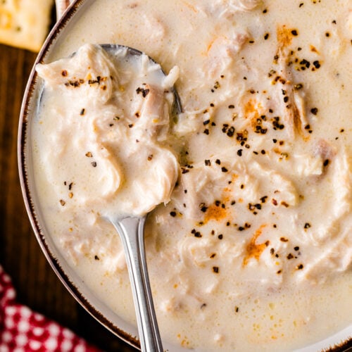 Creamy chicken stew 9 in brown-rimmed bowl with spoon, topped with black pepper and orange zest garnish