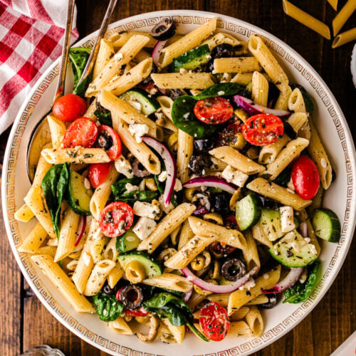 Mediterranean pasta salad 5 with penne, tomatoes, cucumbers, olives, and feta cheese in a decorative white bowl on dark wood