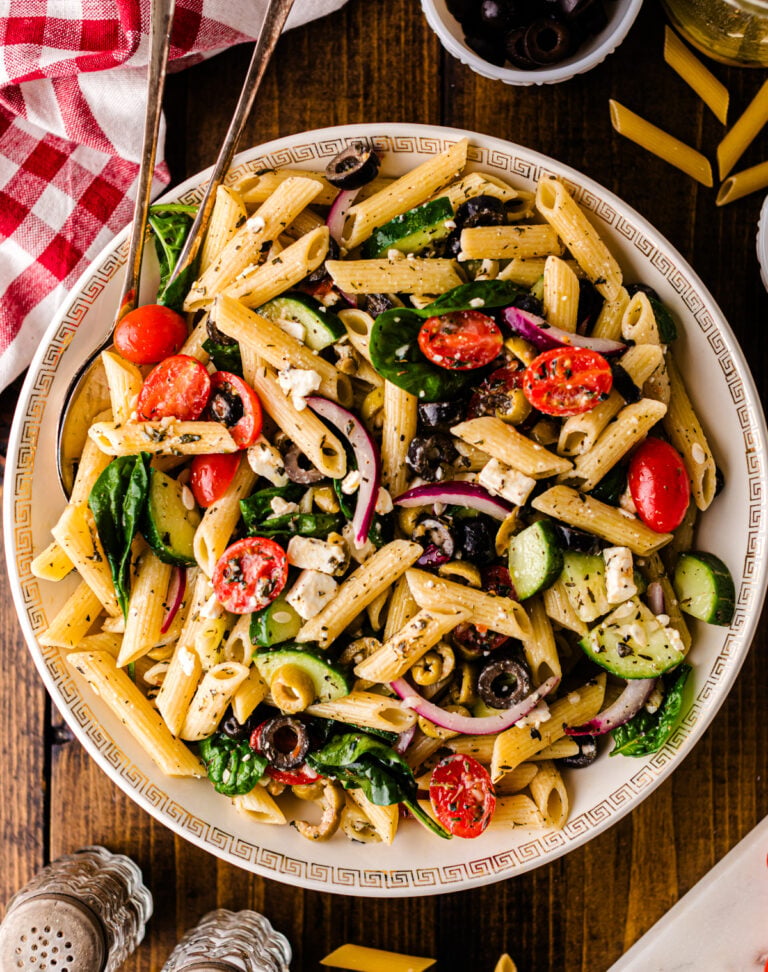 Mediterranean pasta salad 5 with penne, tomatoes, cucumbers, olives, and feta cheese in a decorative white bowl on dark wood