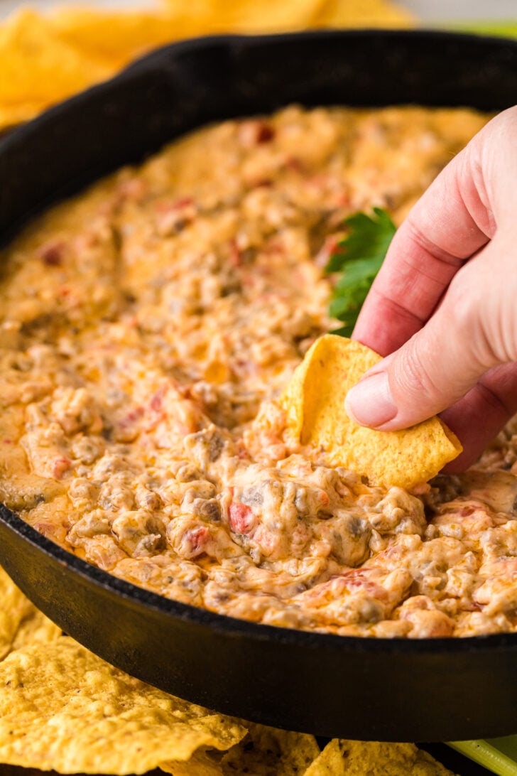 Hand dipping a tortilla chip into hot pimento cheese sausage dip, showing thick, scoopable texture.
