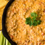 Pimento Cheese and Sausage Dip 5 in black cast iron skillet with tortilla chips and celery sticks on the side, garnished with fresh parsley